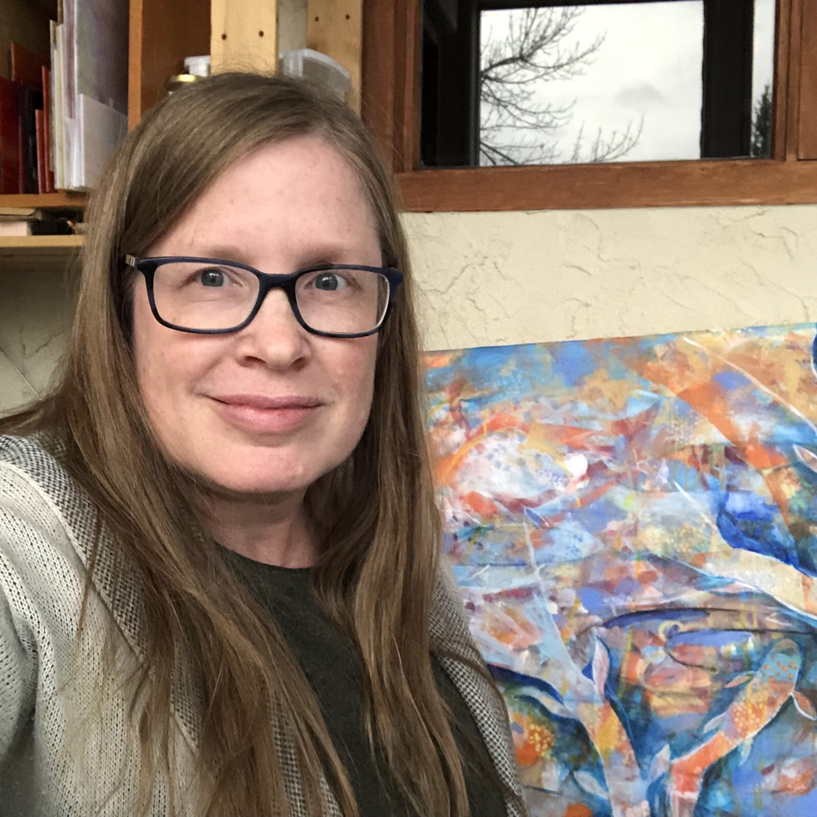 A photo of Deb in her studio with a painting in the background.