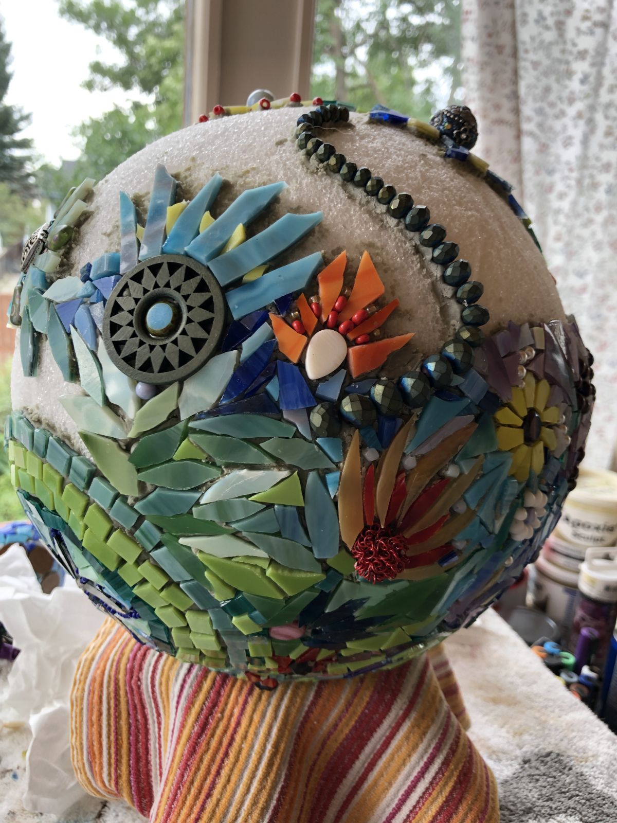 A styrofoam ball partly covered in mosaic flowers and greenery.